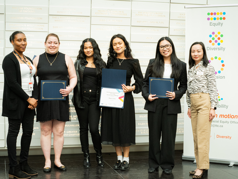 Four-member winning team hold certificates and pose with two TTC officials.